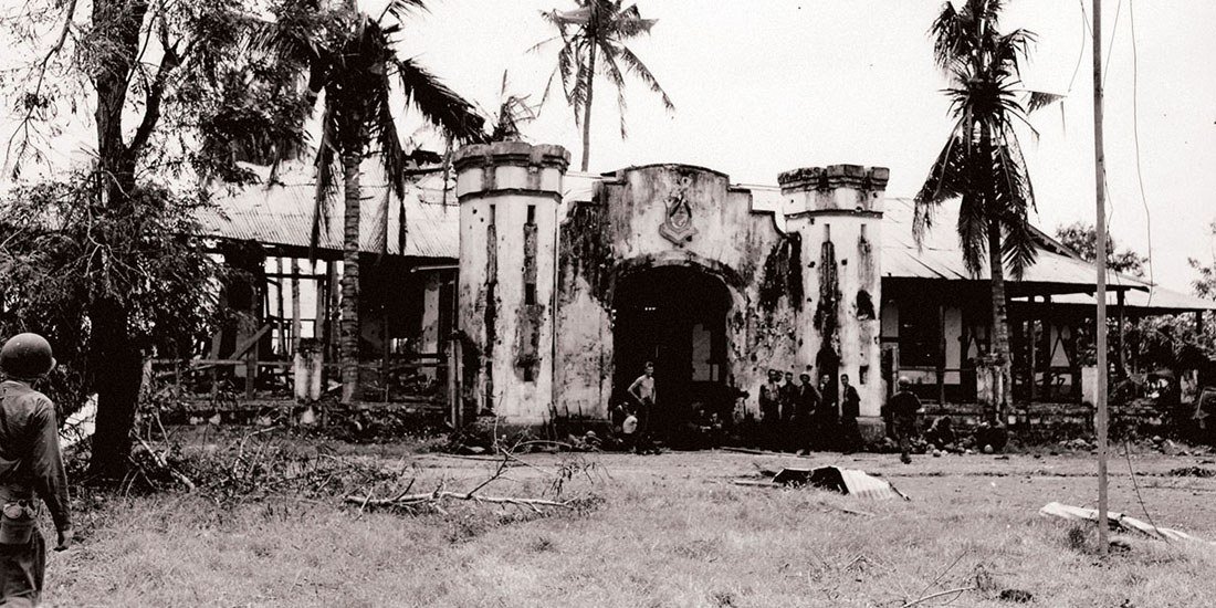 Black-and-white 1945 photograph of the damaged entrance to Camp 10-A at Puerto Princesa, Palawan, after U.S. forces retook the area.