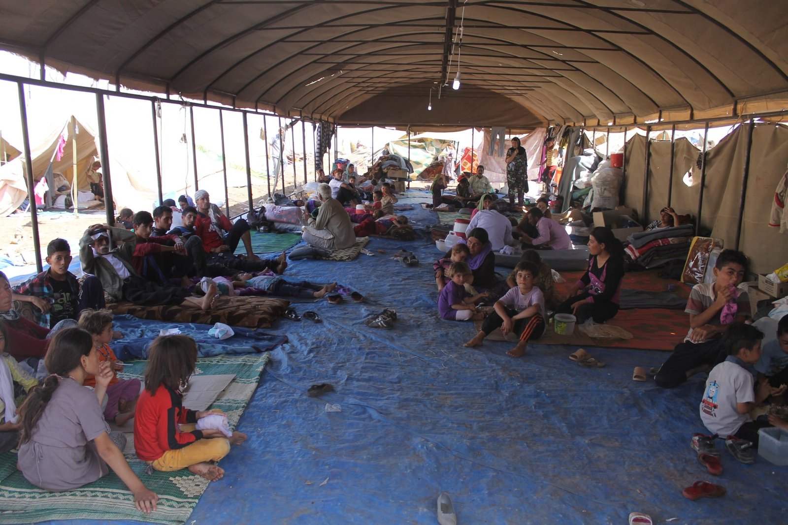 Yazidi families resting beneath a large shelter at Newroz refugee camp in northeastern Syria on 13 August 2014.